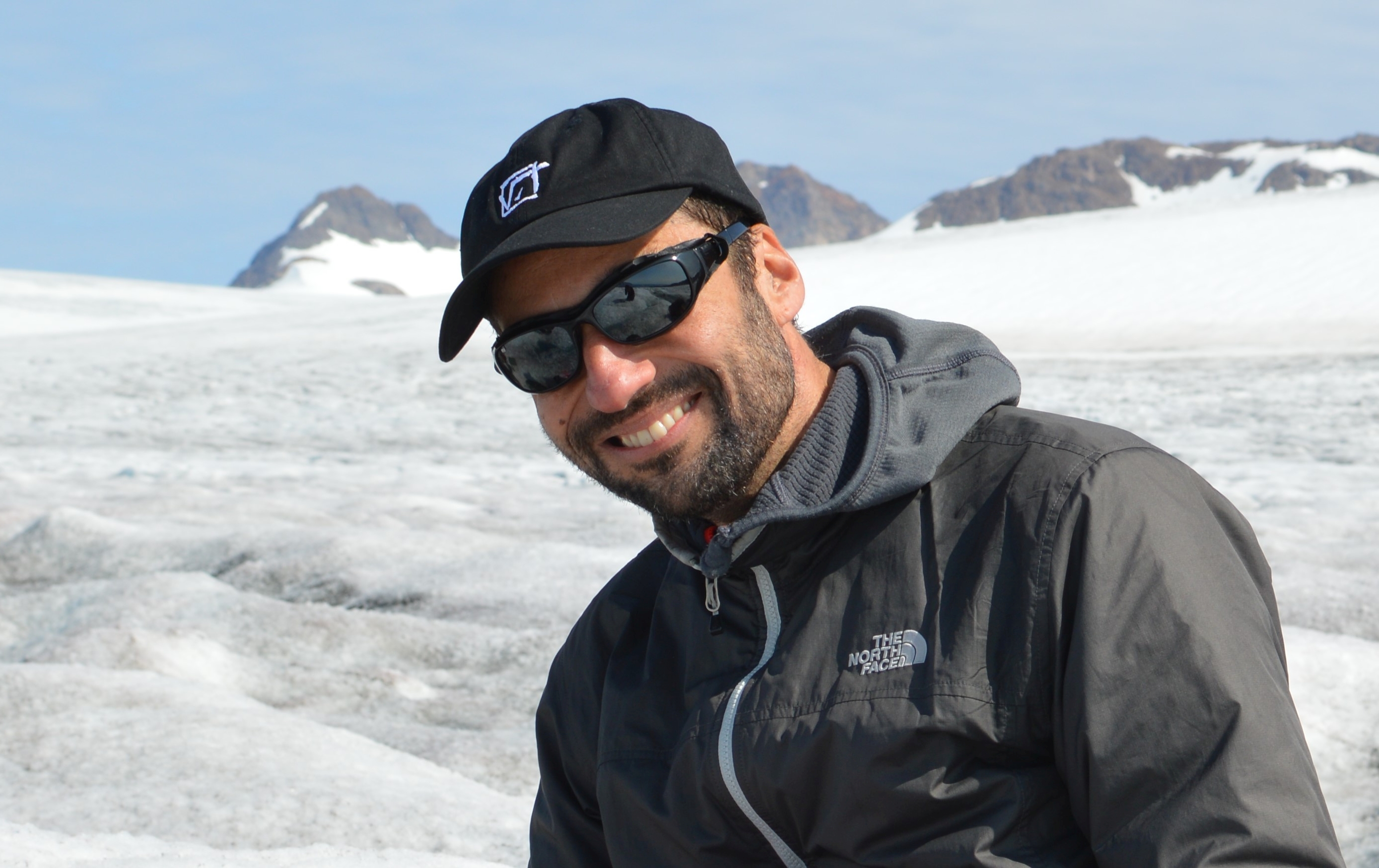 A portrait photo of Alexandre Anesio wearing a cap and sunglasses on the ice in Greenland.